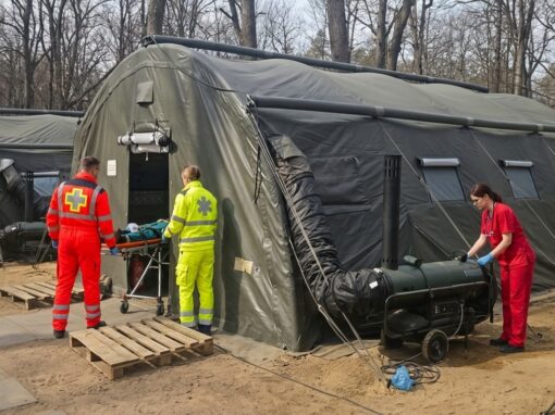Kõrgsurveraamil kiirpüstitatav roheline militaartelk metsasel maastikul, sissepääsu juures on näha soojendusagregaat ja sees põleb soe valgus.